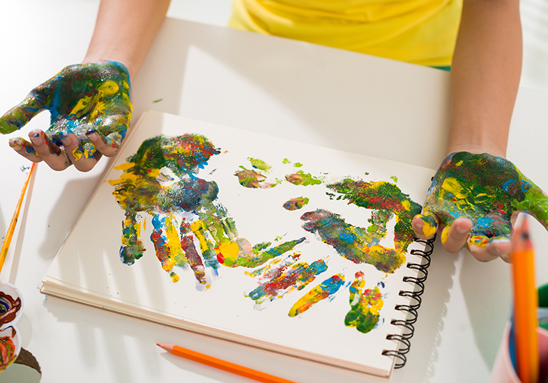 crian&ccedil;a pintando as m&atilde;os e o papel com tintas coloridas