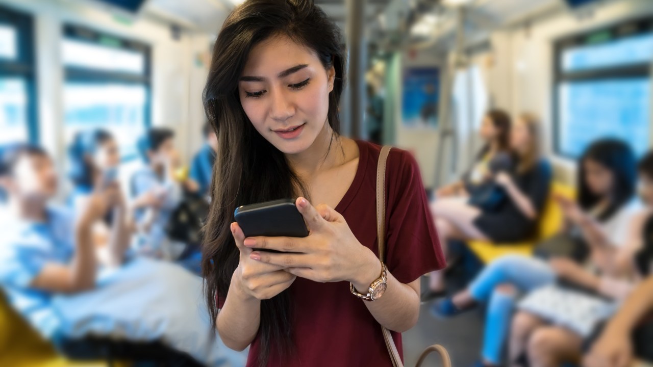 Asian woman passenger with casual suit using the social network via smart mobile phone in the BTS Skytrain rails or MRT subway for travel in the big city, lifestyle and transportation concept