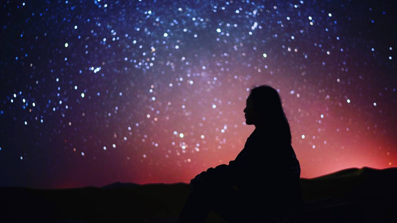 Foto de silhueta de uma pessoa sentada diante de um céu estrelado