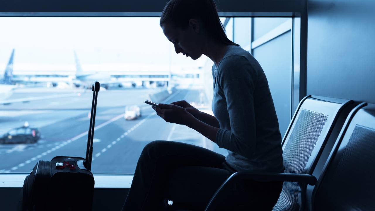 Mulher mexendo no celular no aeroporto.