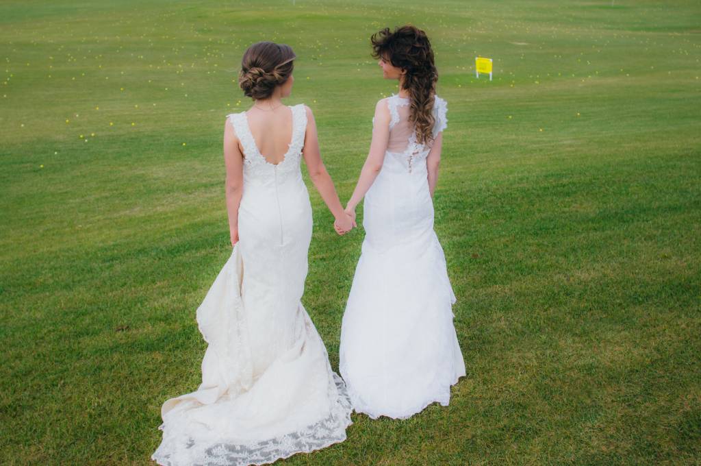 Two beautiful brides holding hands on the green field
