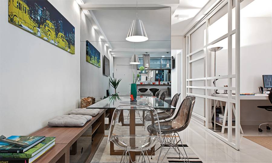<span>A fim de poupar espaço, o arquiteto deu dupla função ao rack, que se prolonga e vira banco. Almofadas demarcam os assentos”, explica. </span>Para não pesar no ambiente, ele escolheu uma mesa com tampo de vidro e base de madeira em cruz. Seguindo a proposta de leveza, as cadeiras são de acrílico incolor e preto. Projeto de Daniel Tesser. <span>A fim de poupar espaço, o arquiteto deu dupla função ao rack, que se prolonga e vira banco. Almofadas demarcam os assentos”, explica. </span>Para não pesar no ambiente, ele escolheu uma mesa com tampo de vidro e base de madeira em cruz. Seguindo a proposta de leveza, as cadeiras são de acrílico incolor e preto. Projeto de Daniel Tesser.