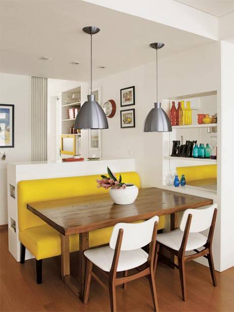 Na &aacute;rea de refei&ccedil;&otilde;es, um sof&aacute; amarelo de couro sint&eacute;tico &eacute; o destaque da decora&ccedil;&atilde;o. Uma mesa de cadeira maci&ccedil;a &eacute; servida por cadeiras, que acrescenta branco &agrave; combina&ccedil;&atilde;o quente. Uma estante embutida, com fundo espelhado, amplia visualmente este canto. Projeto <span>das arquitetas &nbsp;Isabella Lucena e Joanna Fraga.</span>