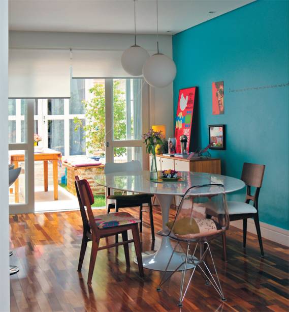 Na casa da designer Ana Maria Mouawad Queiroga, a mesa de jantar recebeu irreverentes cadeiras diferentes. A parede turquesa recebe a ilumina&ccedil;&atilde;o que vem pela porta de vidro (que substitui a janela) e uma cortina rol&ocirc; controla a luminosidade do ambiente.