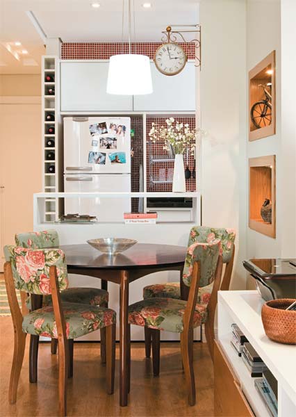 Ao redor da mesa redonda de madeira reúnem-se cadeiras de madeira maciça estofadas com uma charmosa estampa floral. Repare no relógio de parede e também na adega que guarda vinhos no espaço ao lado da geladeira. Projeto da arquiteta Cristiane Dilly. Ao redor da mesa redonda de madeira reúnem-se cadeiras de madeira maciça estofadas com uma charmosa estampa floral. Repare no relógio de parede e também na adega que guarda vinhos no espaço ao lado da geladeira. Projeto da arquiteta Cristiane Dilly.