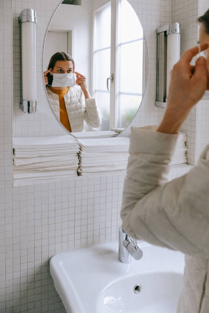 cuidados-manuseio-produtos-limpeza-máscara-luvas Mulher em seu banheiro colocando uma máscara de proteção