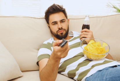 Homem no sofá com salgadinhos e refrigerante