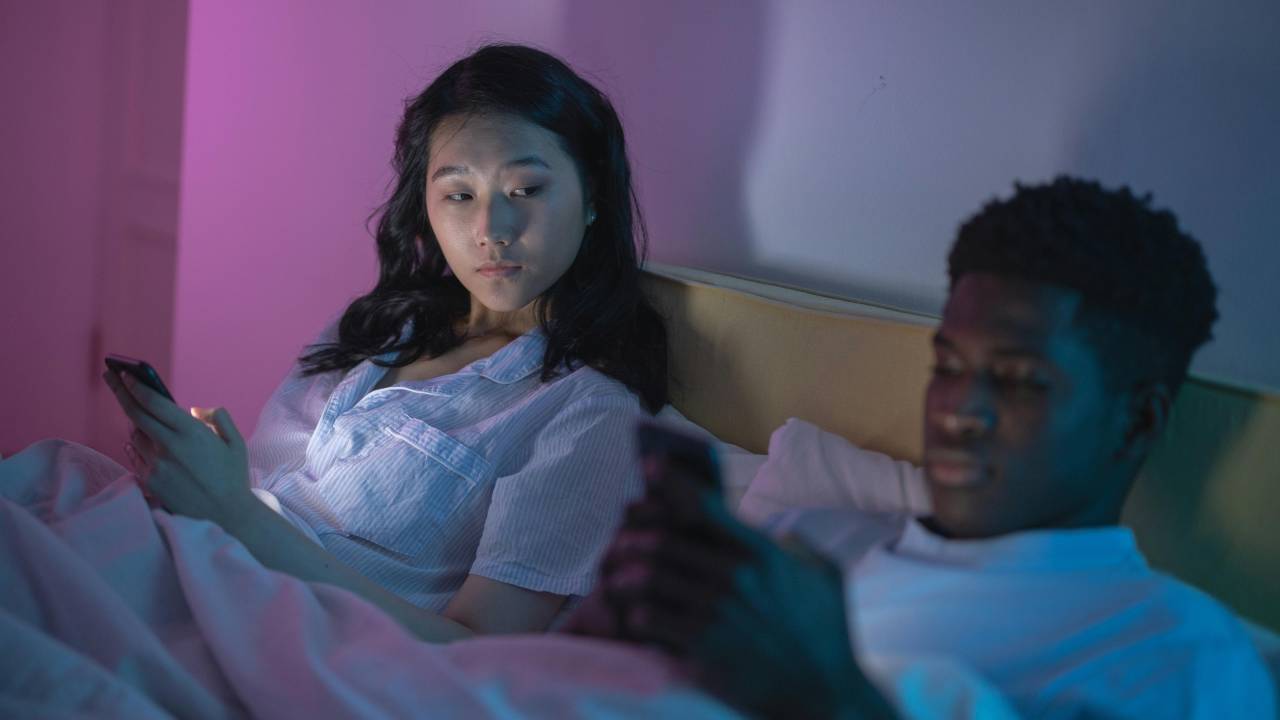 Mulher olhando para o celular do marido, que está ao seu lado, com ciúme