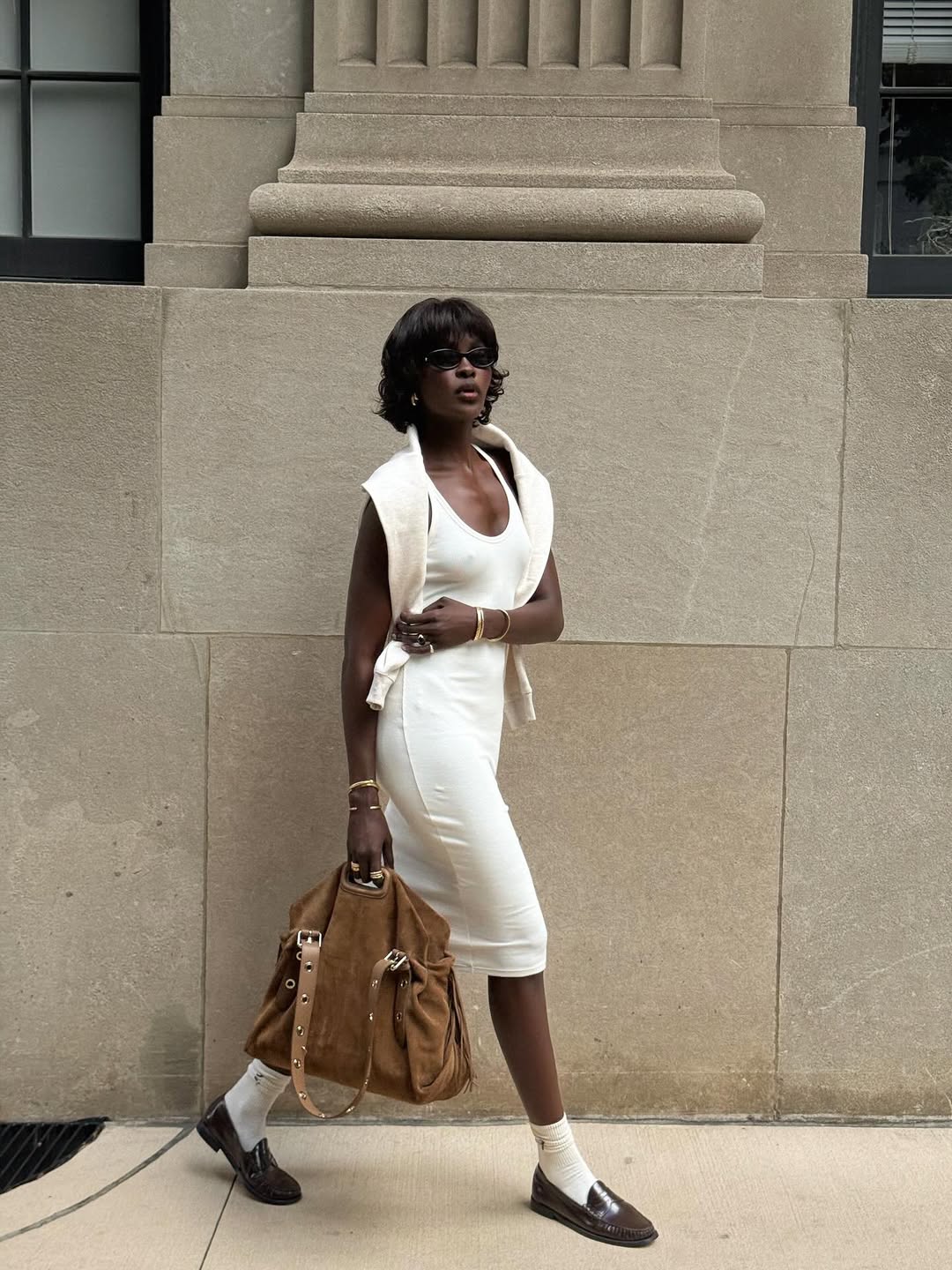 Foto de uma mulher negra usando um look composto por vestido branco, su&eacute;ter branco, bolsa marrom e sapato