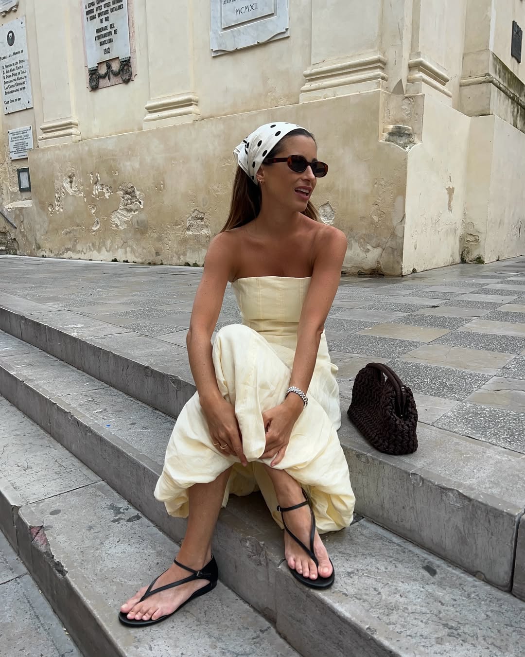 Foto de uma mulher branca usando um look composto por vestido branco, len&ccedil;o na cabe&ccedil;a, &oacute;culos de sol e sand&aacute;lia