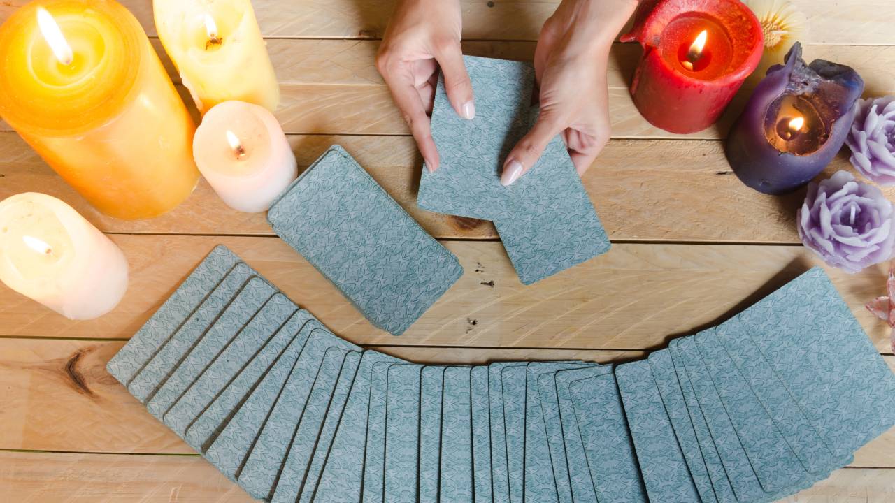 Tarô da semana: mãos femininas lendo cartas de tarô em uma mesa clara de madeira.