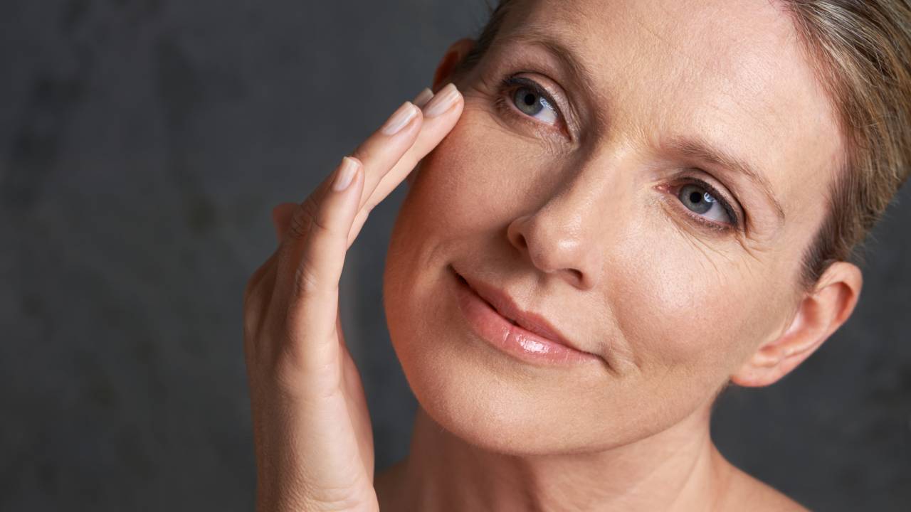 Mulher passando cremes no rosto, em alusão ao conteúdo de como fazer skincare durante a menopausa