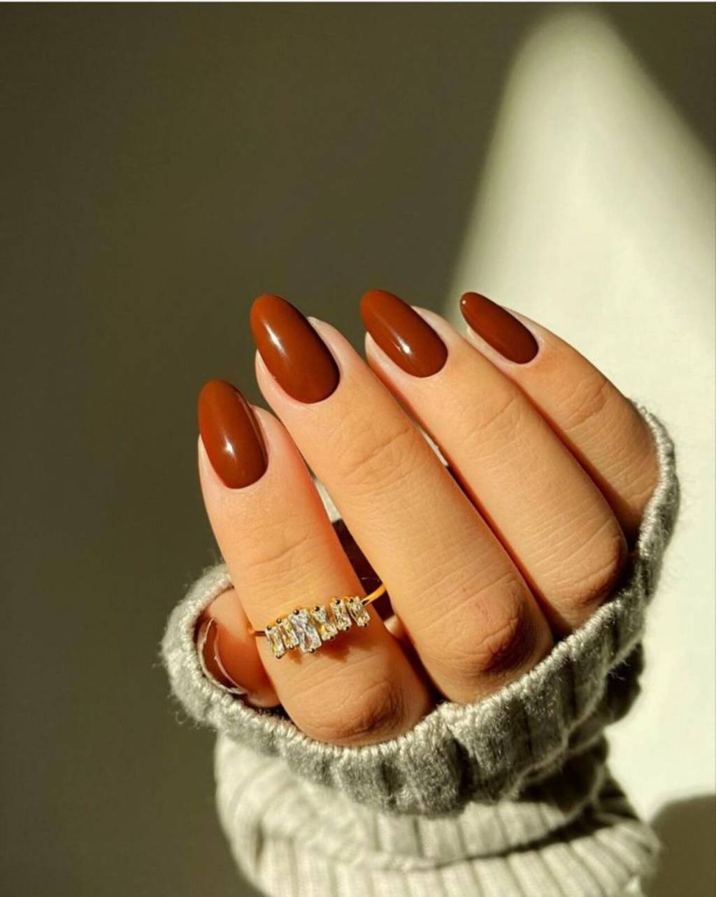 tons-unhas-inverno (16) Imagem de mão branca com unhas amendoadas com esmaltação laranja queimado.
