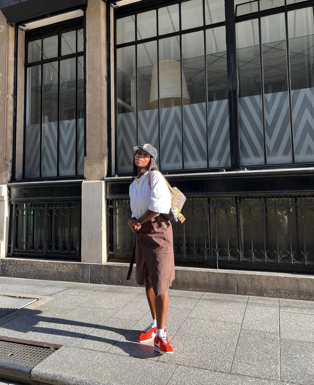 Look com saia utilit&aacute;ria marrom, camiseta branca e t&ecirc;nis vermelho