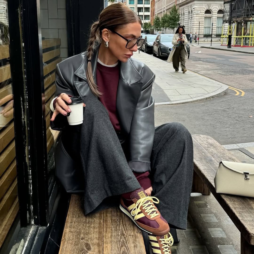 Foto de uma mulher usando um look composto por jaqueta de couro preta, cal&ccedil;a preta e t&ecirc;nis marrom