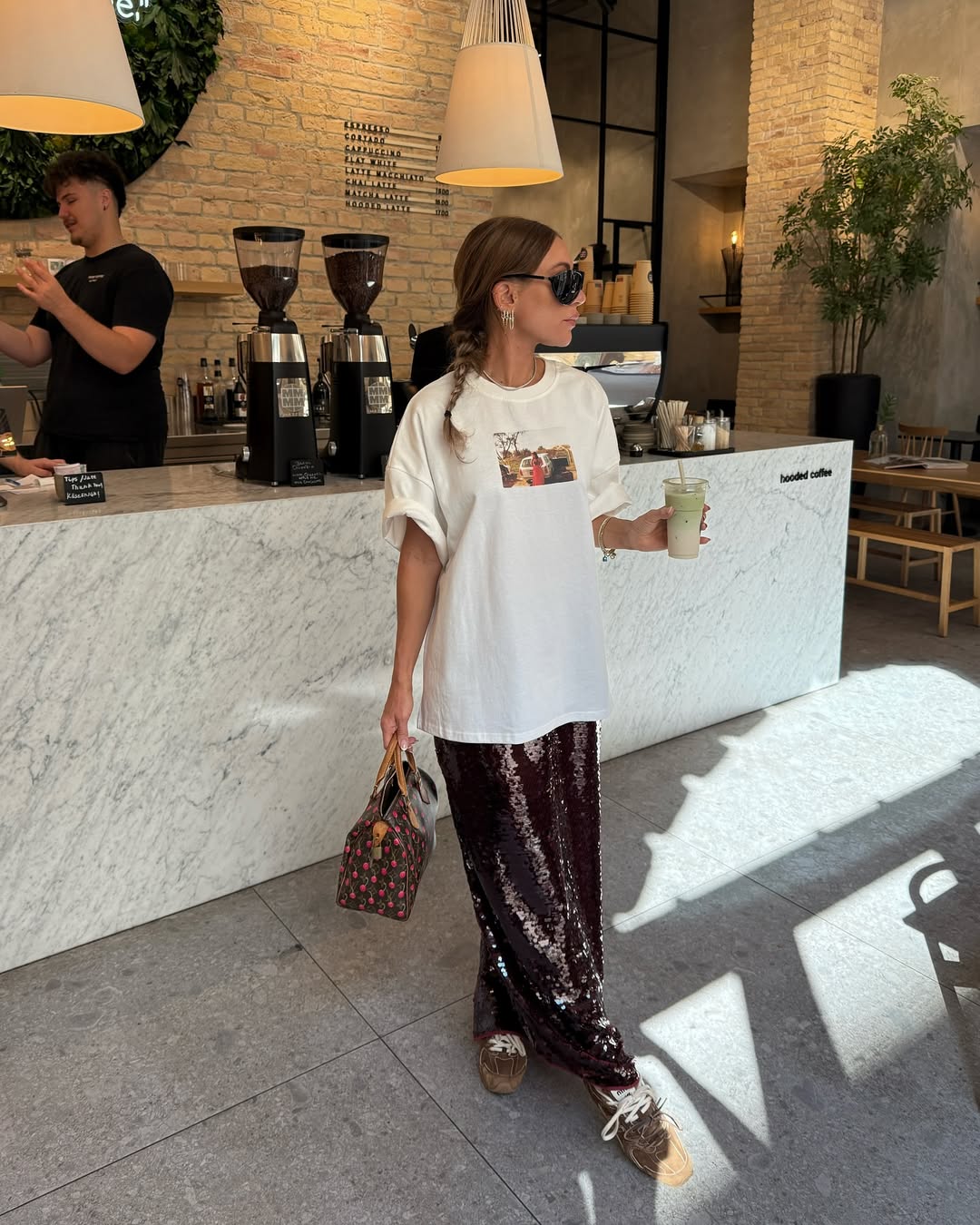 Foto de uma mulher morena usando um look composto por camiseta branca, saia com brilhos marrom e t&ecirc;nis marrom