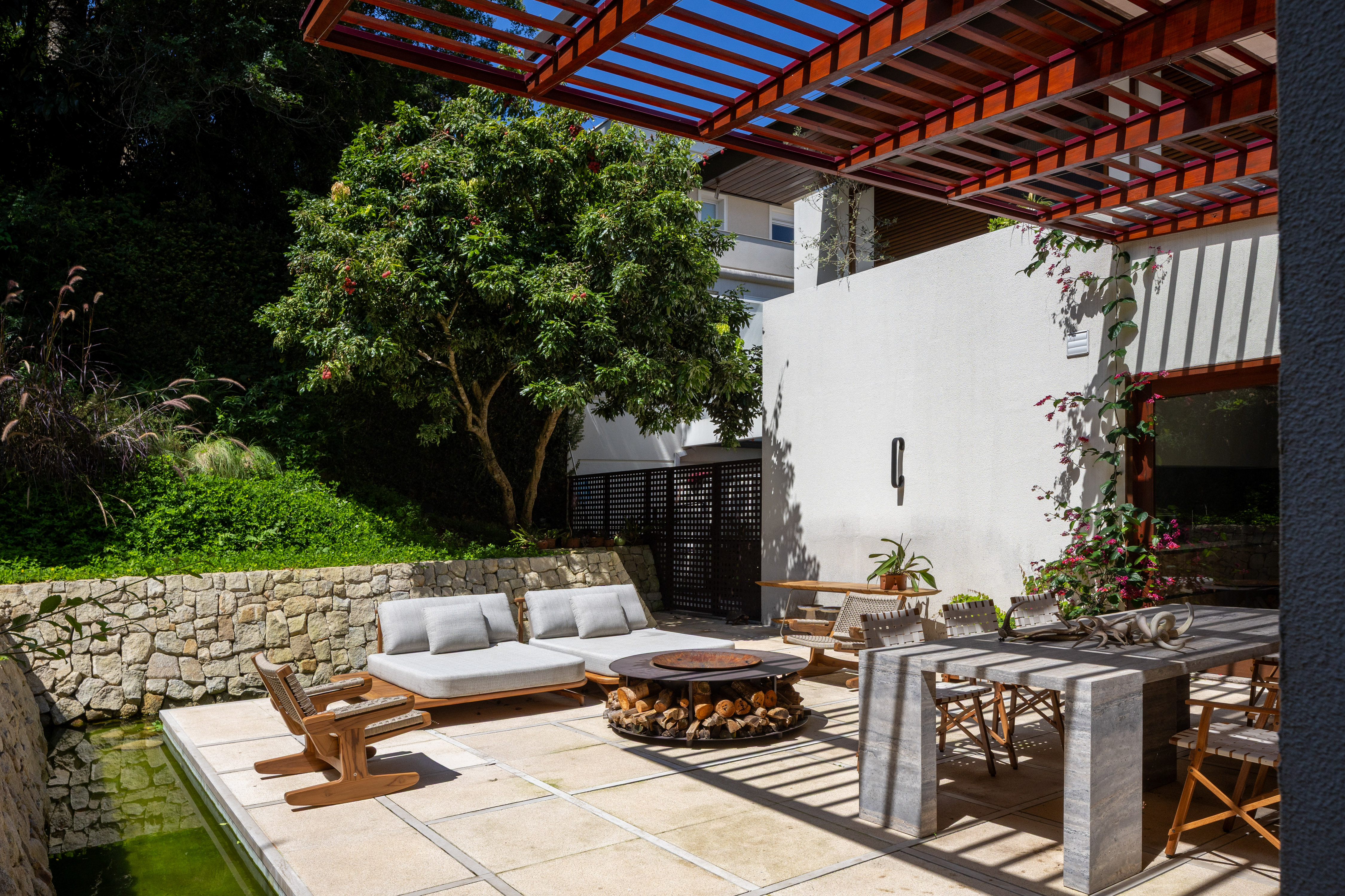 Com pergolado retr&aacute;til e lareira central, o espa&ccedil;o conecta os blocos da casa em torno da conviv&ecirc;ncia.