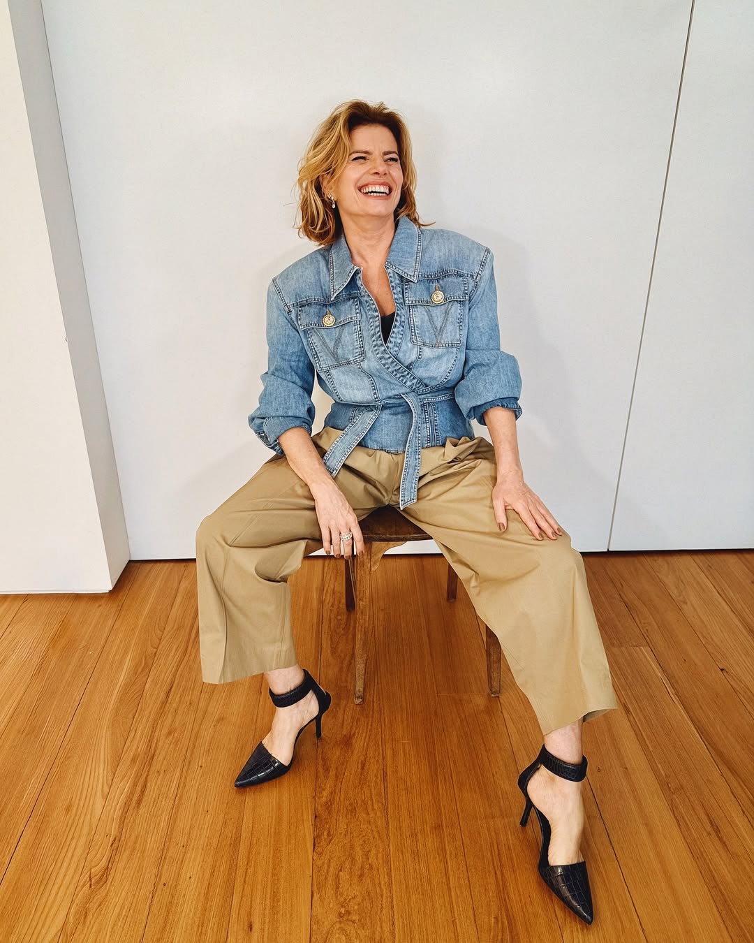 Foto de Debora Bloch usando um look composto por jaqueta jeans, cal&ccedil;a de alfaiataria marrom e salto scarpin preto