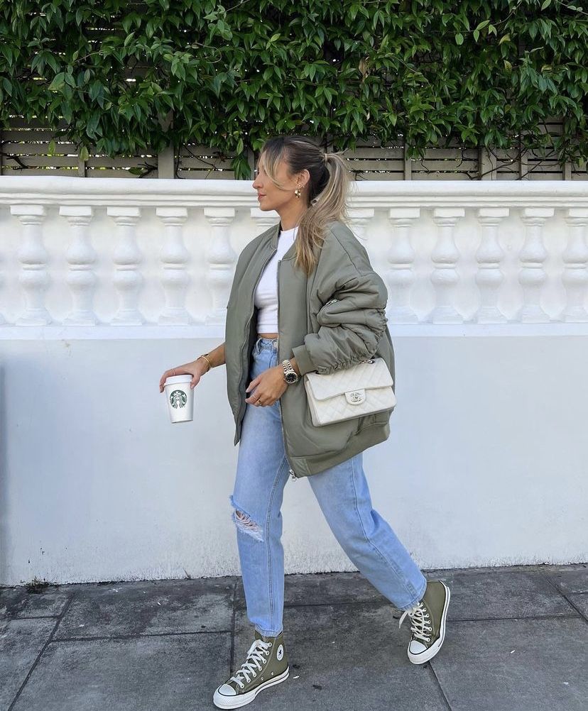 Foto de uma mulher loira usando um look composto por regata branca, jaqueta verde, cal&ccedil;a jeans e t&ecirc;nis All Star verde pistache