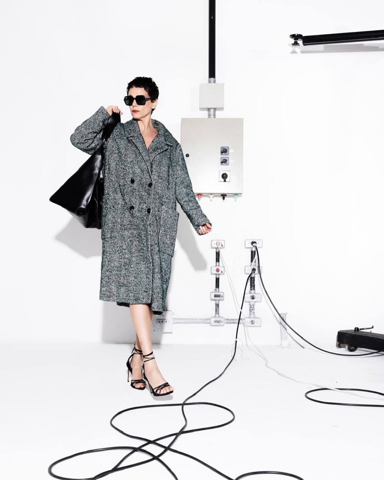 Foto de Malu Galli usando um look composto por trench coat cinza, bolsa preta longa, &oacute;culos de sol pteto e salto preto