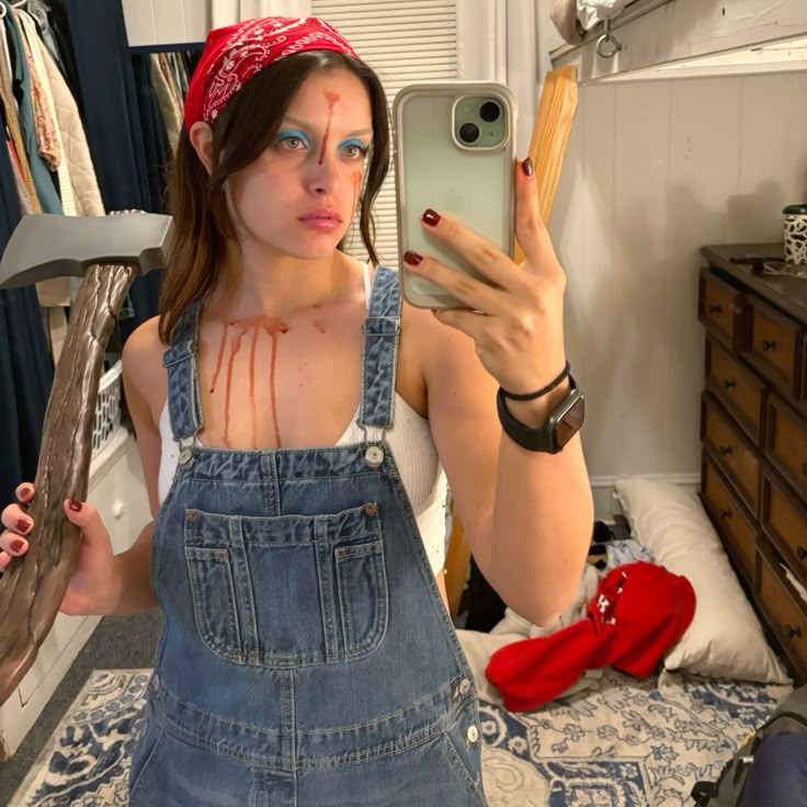 antasia inspirada no filme 'Maxine', com jardineira jeans, camiseta listrada e maquiagem sangrenta