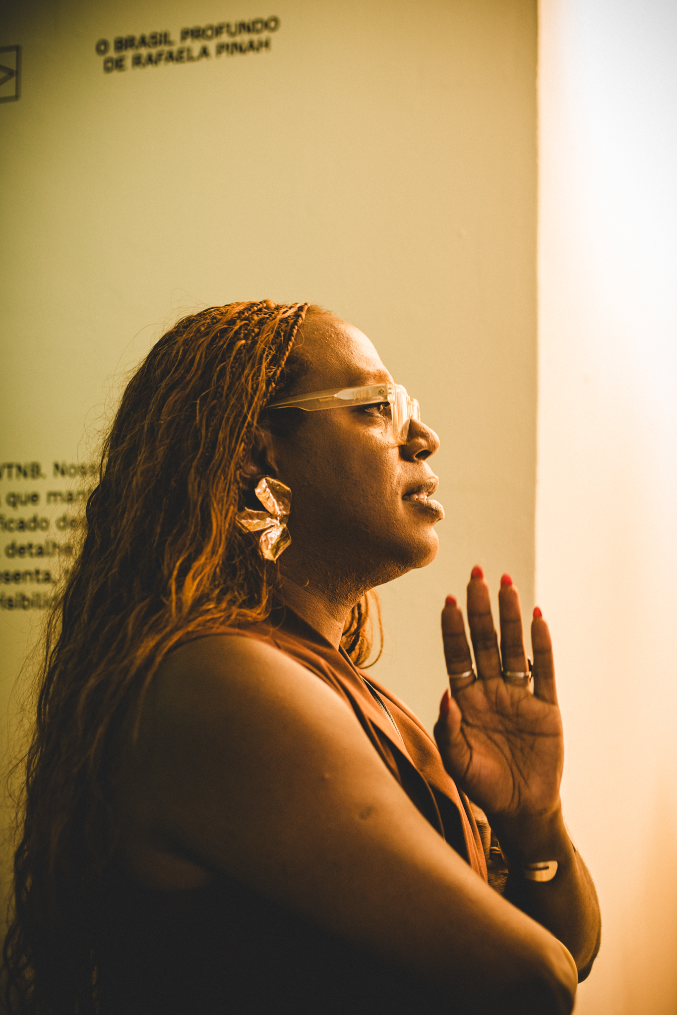 Foto de Rafaela Pinah. Ela &eacute; negra, est&aacute; de lado, usando tran&ccedil;as, e com a m&atilde;o levantada