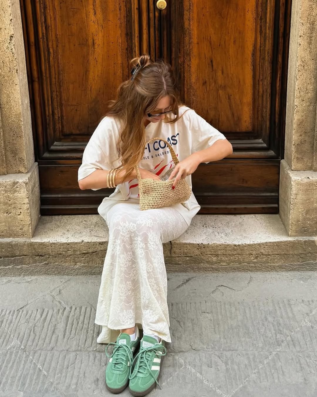 Foto de uma mulher ruiva usando um look composto por camiseta, saia branca e t&ecirc;nis verde. Ela tamb&eacute;m est&aacute; com uma bolsa bege