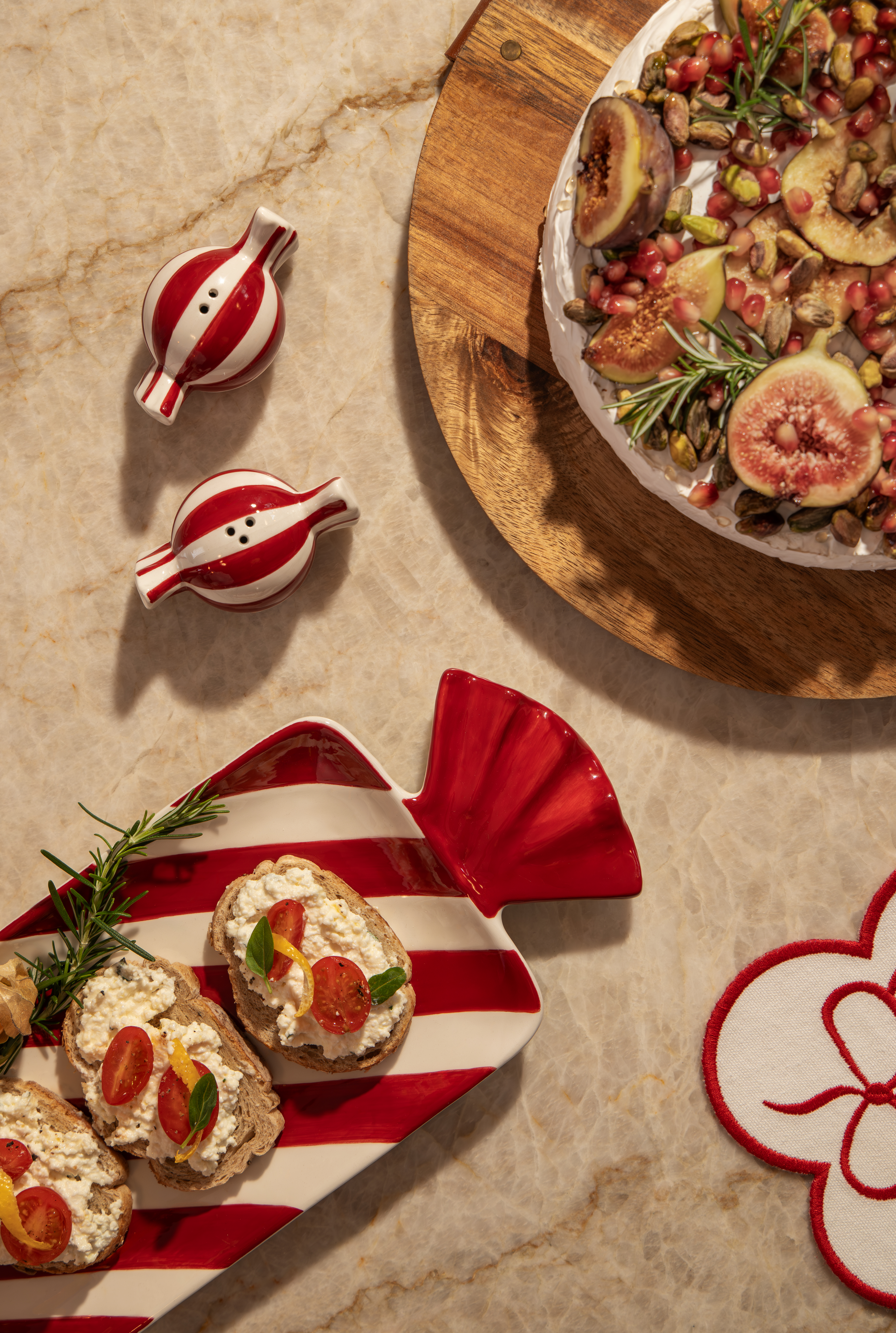 Mesa posta natalina com enfeites vermelhos e brancos da Casa Riachuelo da Oscar Freire em S&atilde;o Paulo, incluindo petisqueira em formato de bala, porta-temperos listrados e aperitivos decorados. Foto destaca itens acess&iacute;veis da cole&ccedil;&atilde;o de Natal da Casa Riachuelo para cozinha e mesa posta