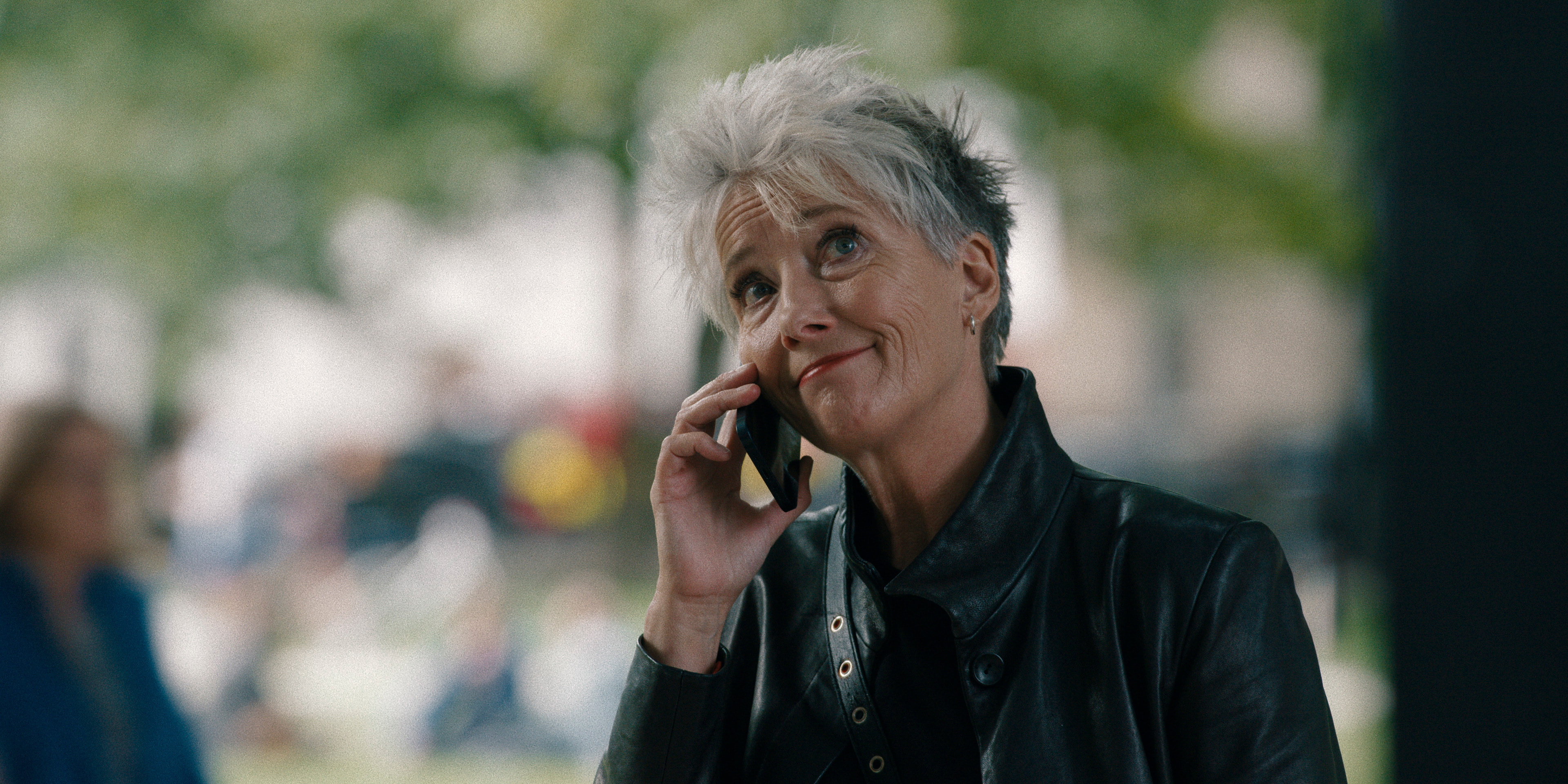Mulher grisalha de cabelo curto e jaqueta preta olhando para cima enquanto fala no telefone.