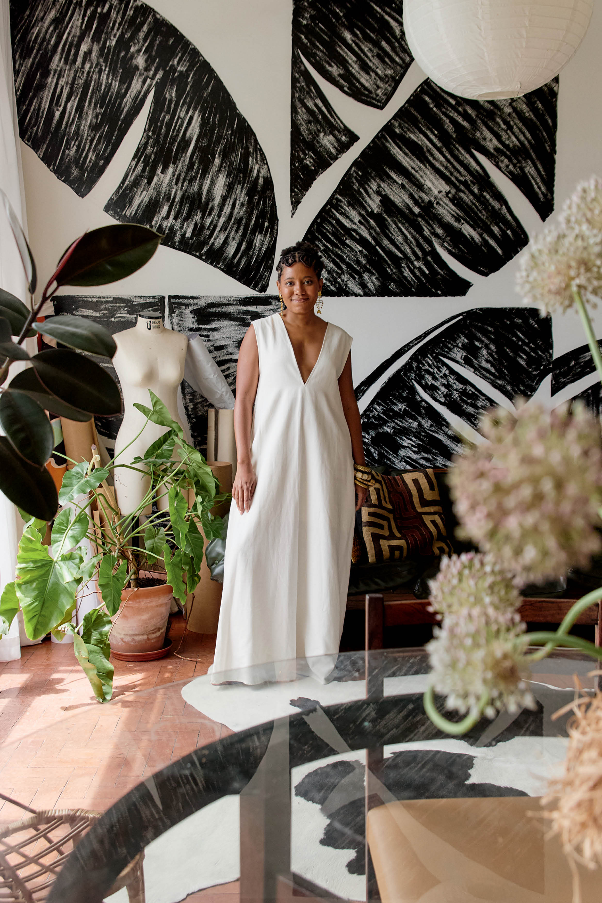 mulher de vestido branco em p&eacute; em frente &agrave; parede com estampa de folha de bananeira
