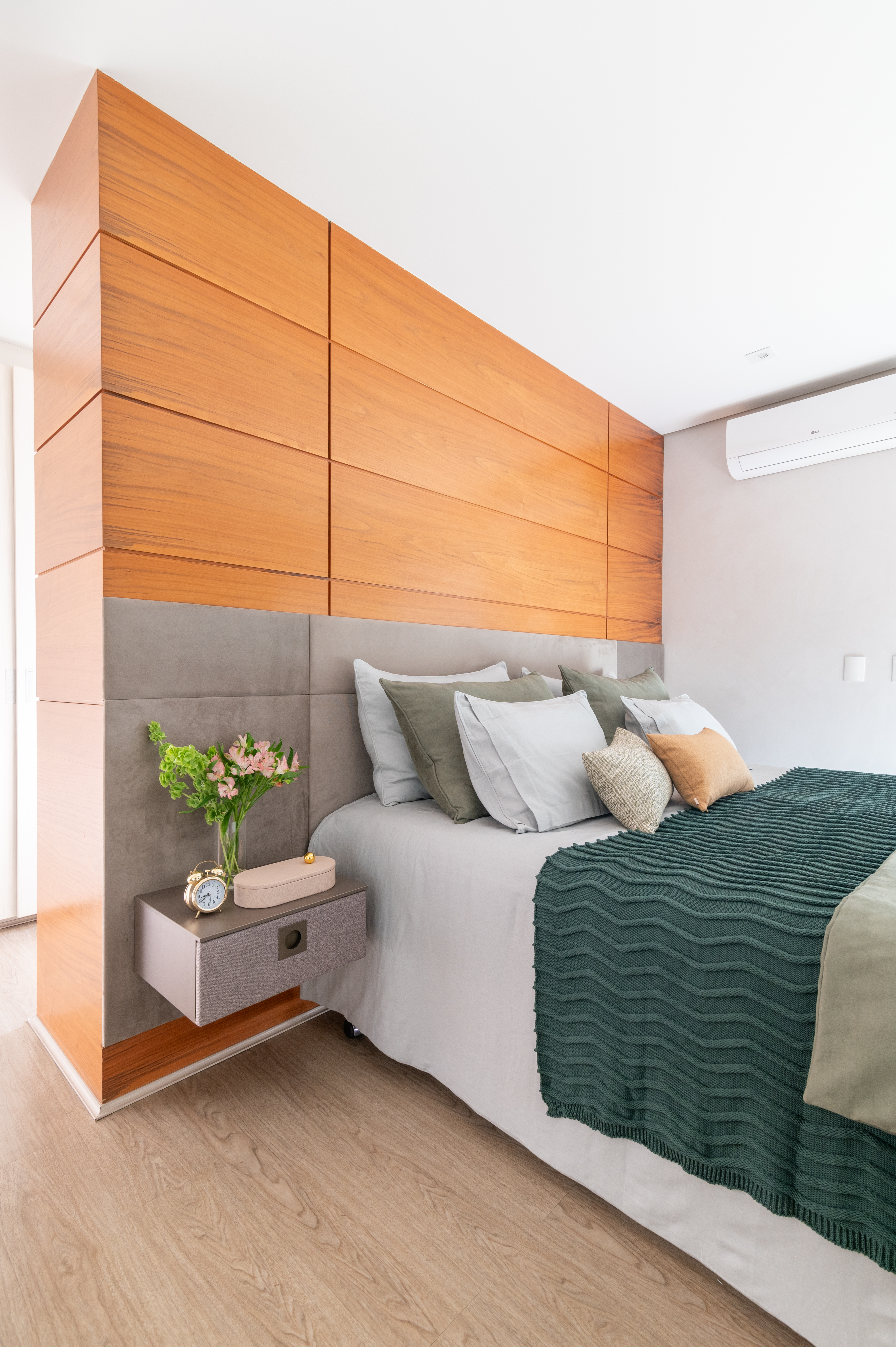 Quarto de casal com parede de madeira, roupa de cama em cores neutras e verde.