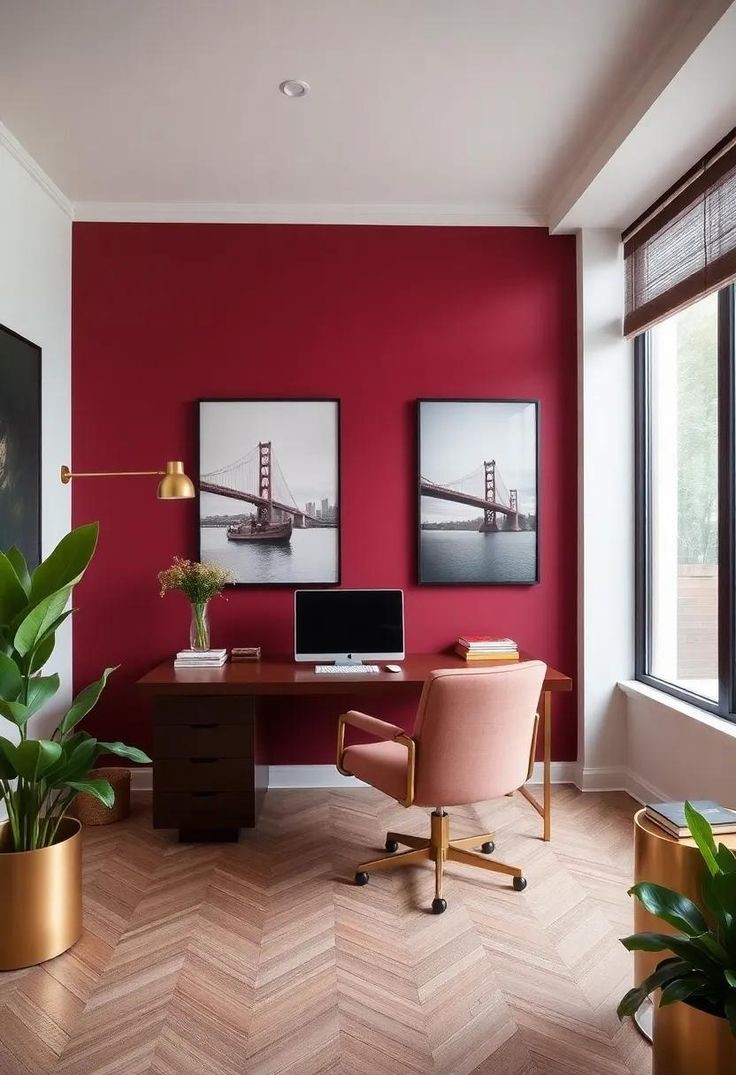 Sala de home office com parede Cherry Red, mesa de madeira e cadeira rosada, complementado por quadros, plantas e lumin&aacute;ria dourada. A imagem demonstra como o vermelho-cereja pode estimular criatividade e foco na decora&ccedil;&atilde;o do escrit&oacute;rio
