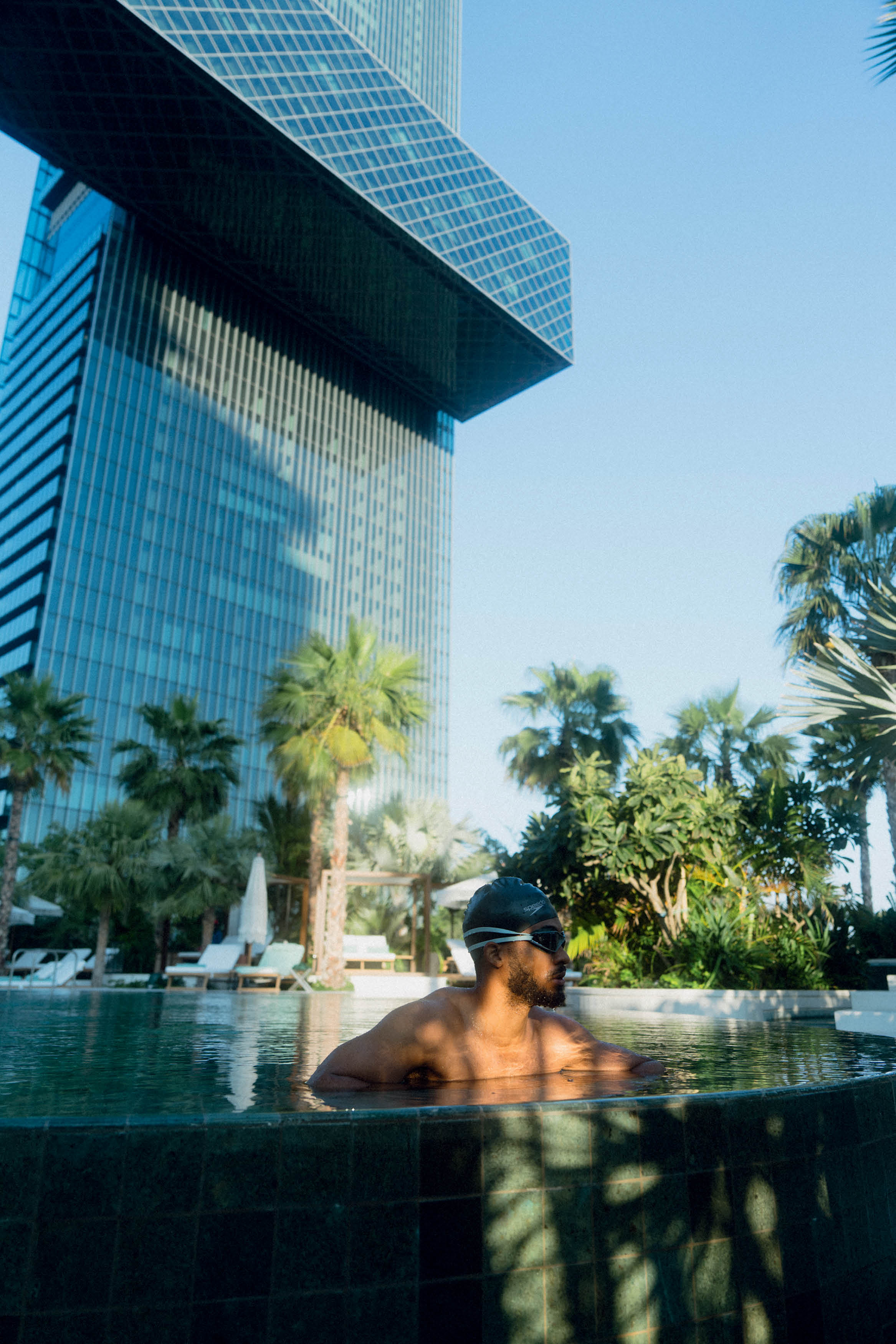 Homem em piscina externa de hotel usando touca e &oacute;culos de nata&ccedil;&atilde;o.