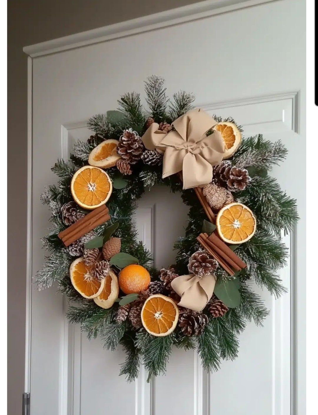 Imagem de guirlanda laranja, com fatias da fruta laranja, galhos de pinheiro, flores com neve fake, pinhos e canela em pau.