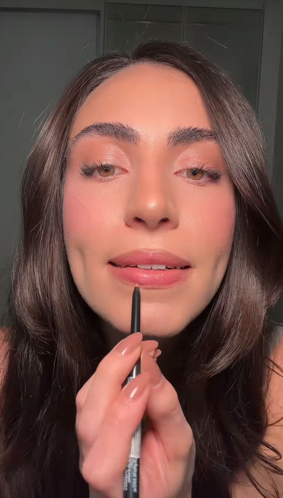 mulher de cabelo castanho maquiada passando l&aacute;pis de boca