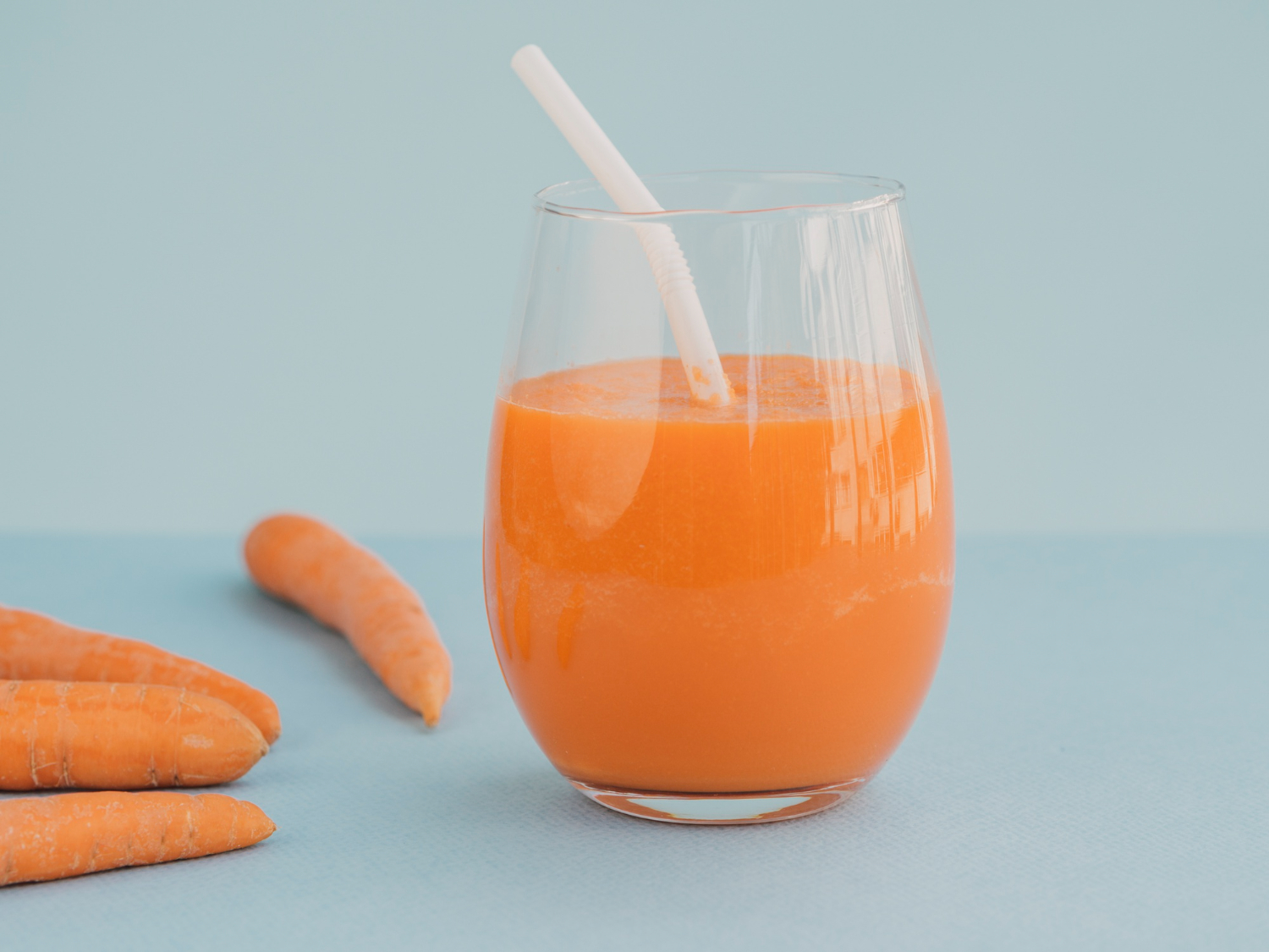 Shot de imunidade de cenoura, laranja e gengibre em copo de vidro com palha, com cenouras frescas ao lado. A cor laranja vibrante destaca a receita rica em Vitamina C e betacaroteno para fortalecer a imunidade e desintoxicar.