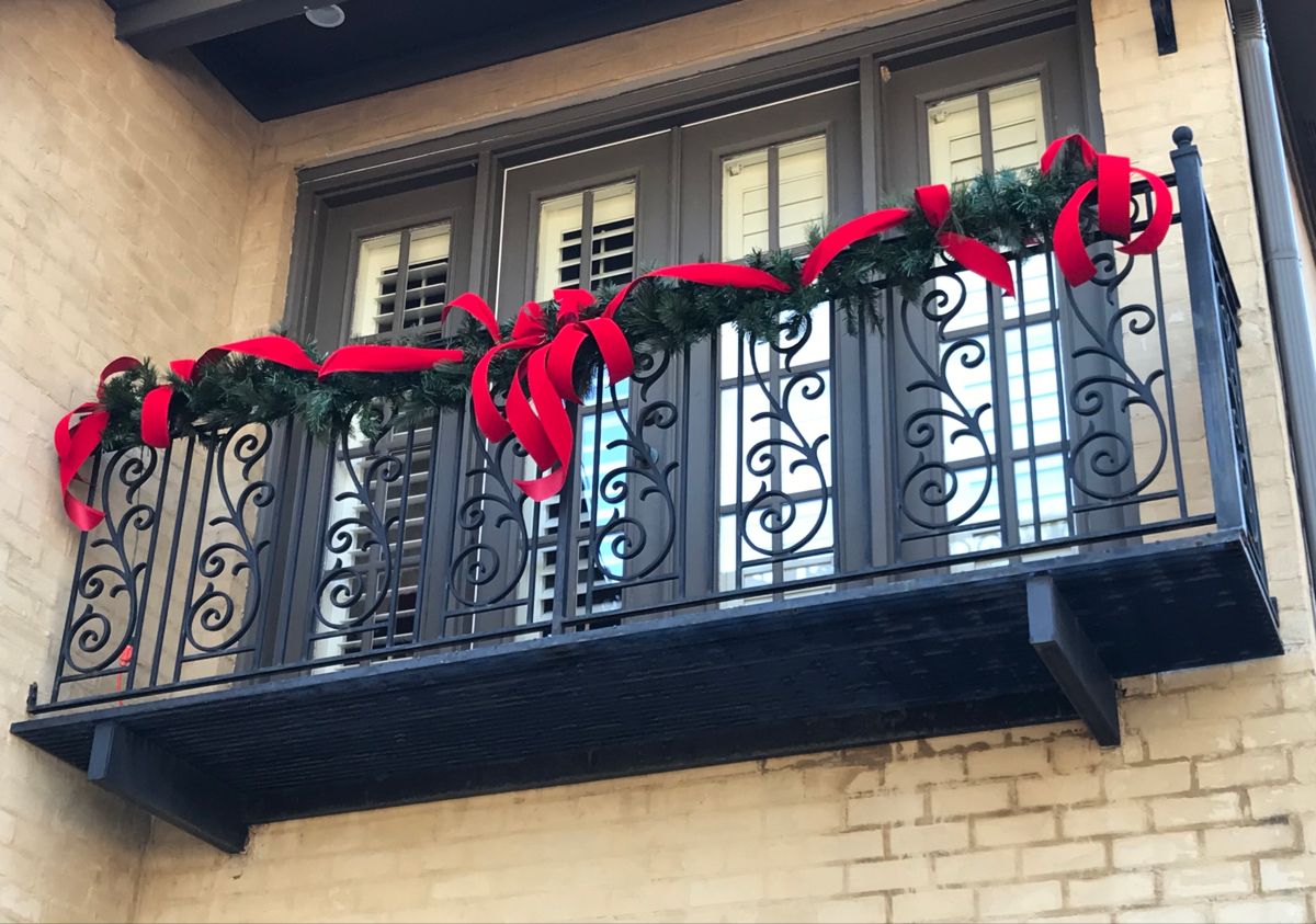 Varanda de pr&eacute;dio decorada com fest&otilde;es e la&ccedil;o vermelho.