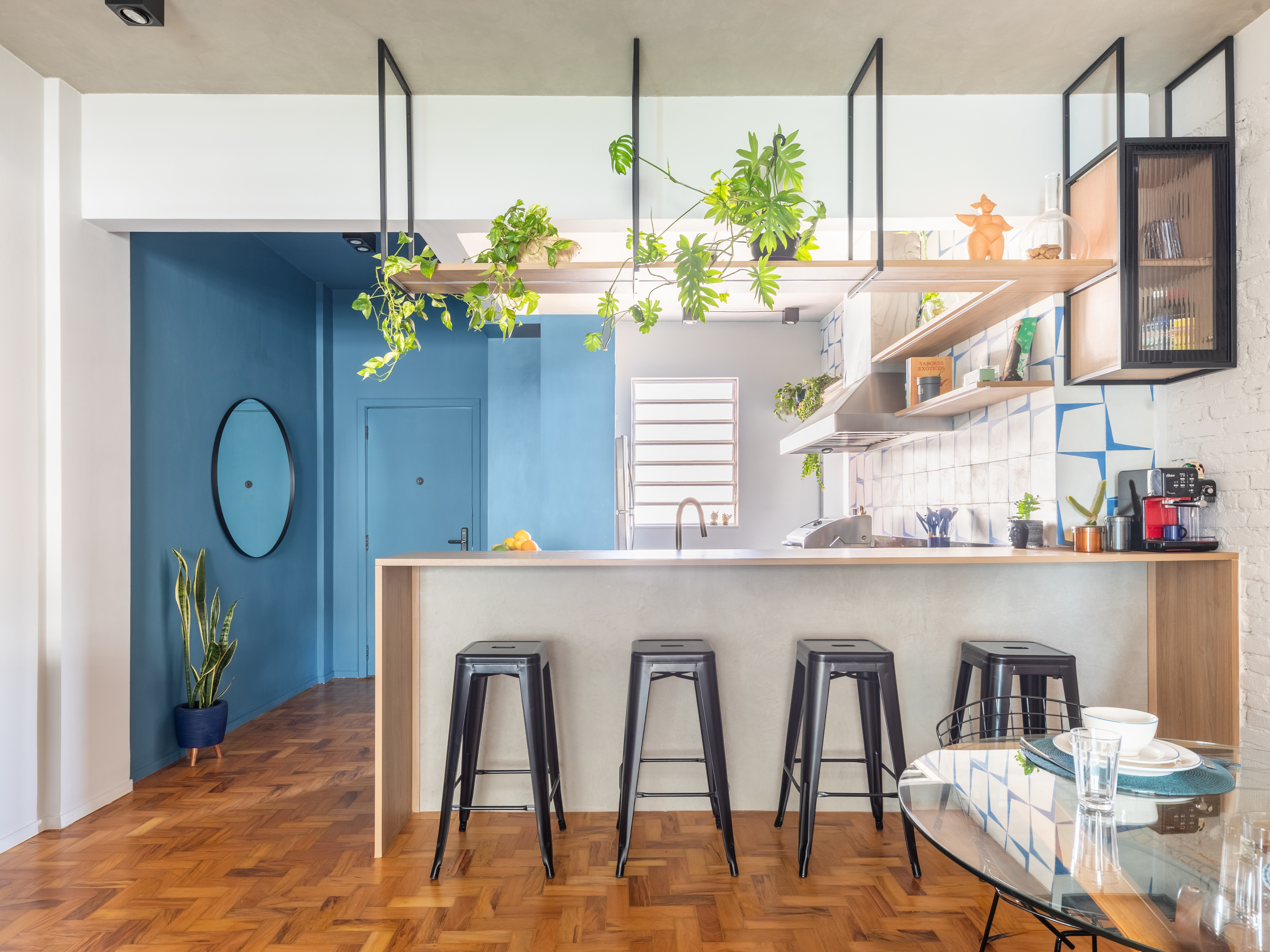 Cozinha americana pequena com piso de taco, vasos suspensos e bancada com bancos pretos met&aacute;licos