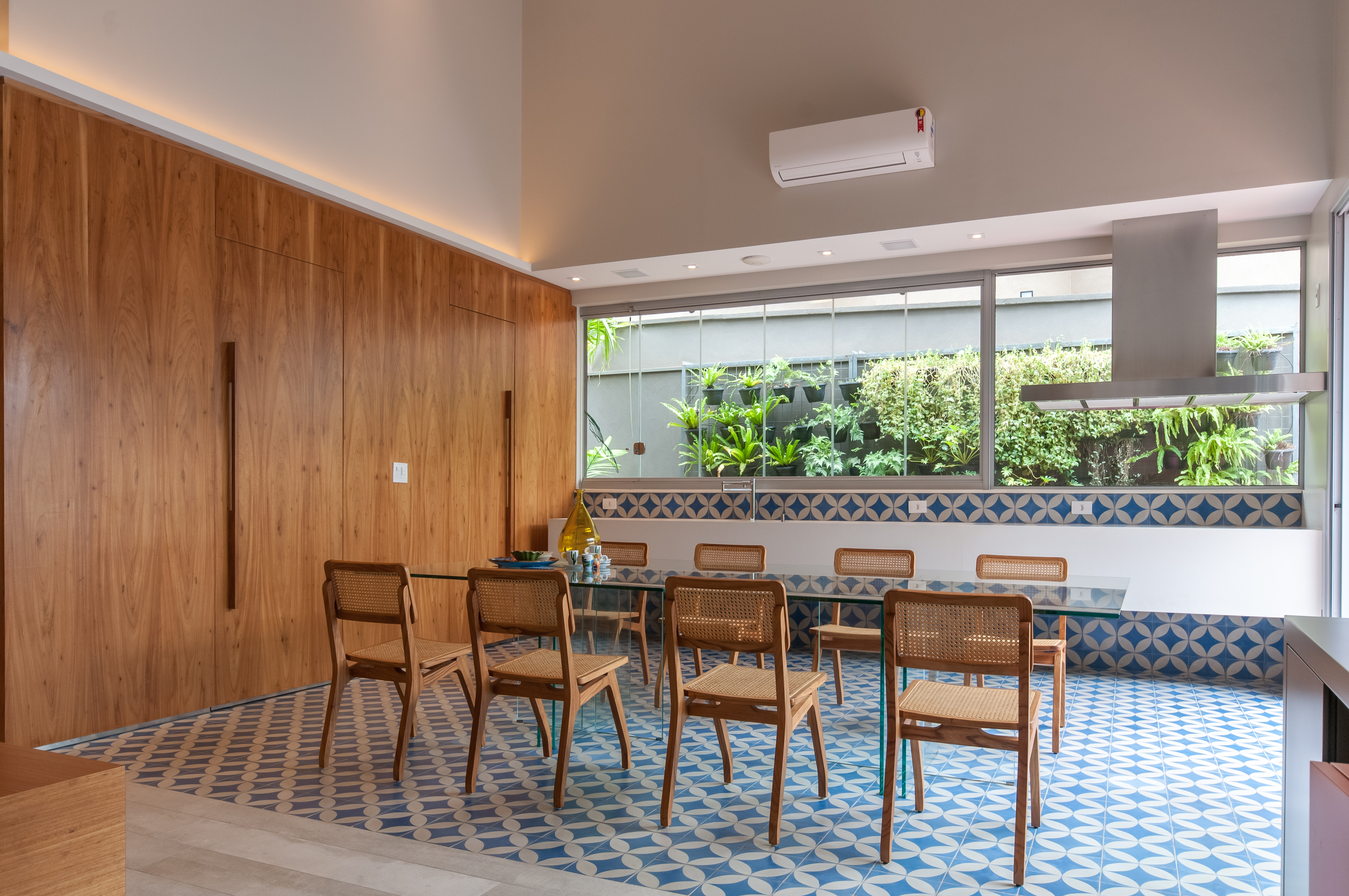 Sala de estar com parede de madeira, grande mesa de vidro e piso de ladrilho azul