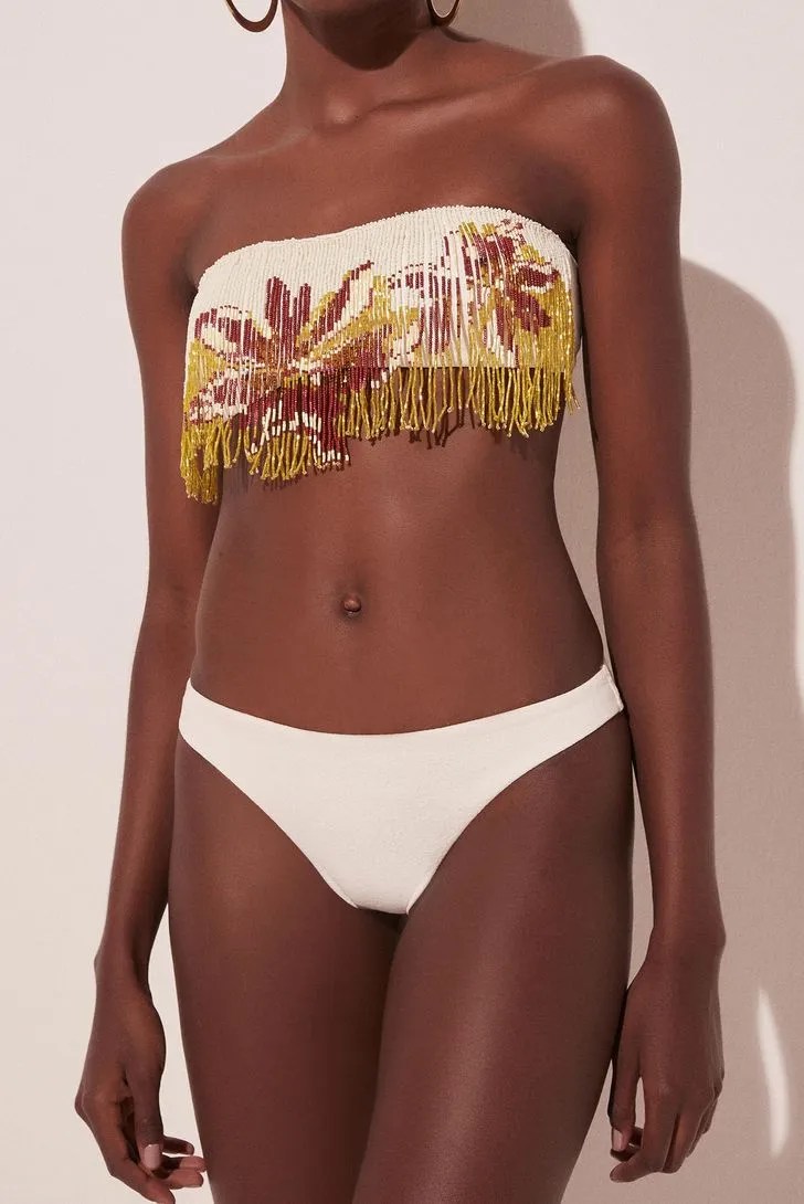 Foto de um biqu&iacute;ni com aplica&ccedil;&otilde;es feitas &agrave; m&atilde;o. Quem usa a pe&ccedil;a &eacute; uma mulher com pele negra