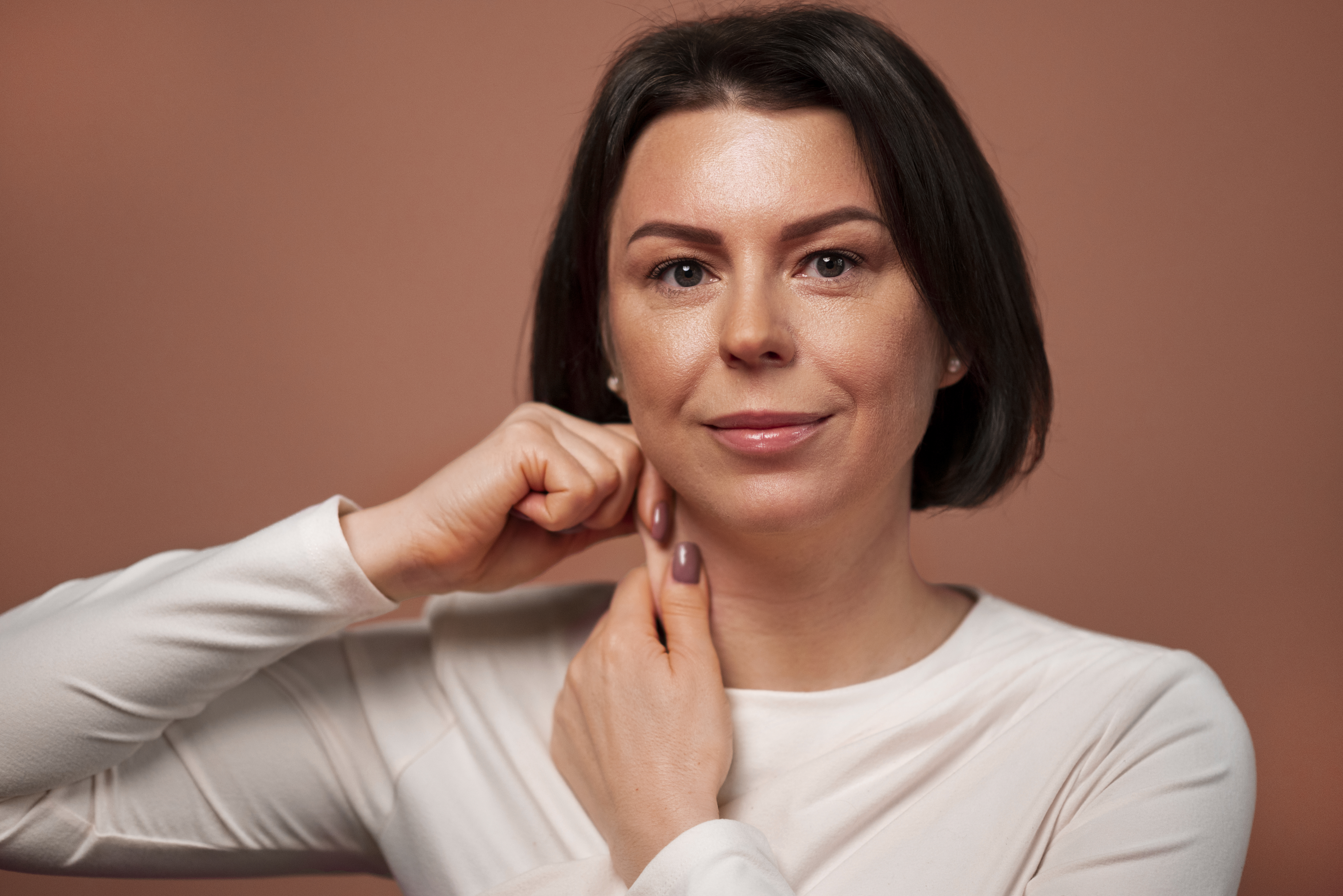 Imagem de mulher morena tocando a pele do pesco&ccedil;o, sinalizando &aacute;rea que deve ser rejuvenescida.