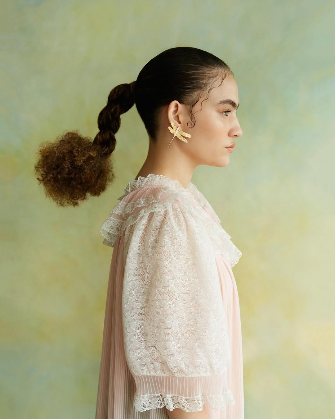 Foto de uma mulher de lado usando uma bata branca e um brinco com formato de inseto