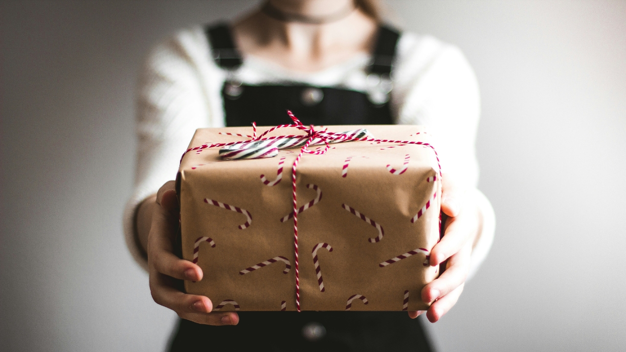 Foto de mulher entregando presente de natal em direção à câmera