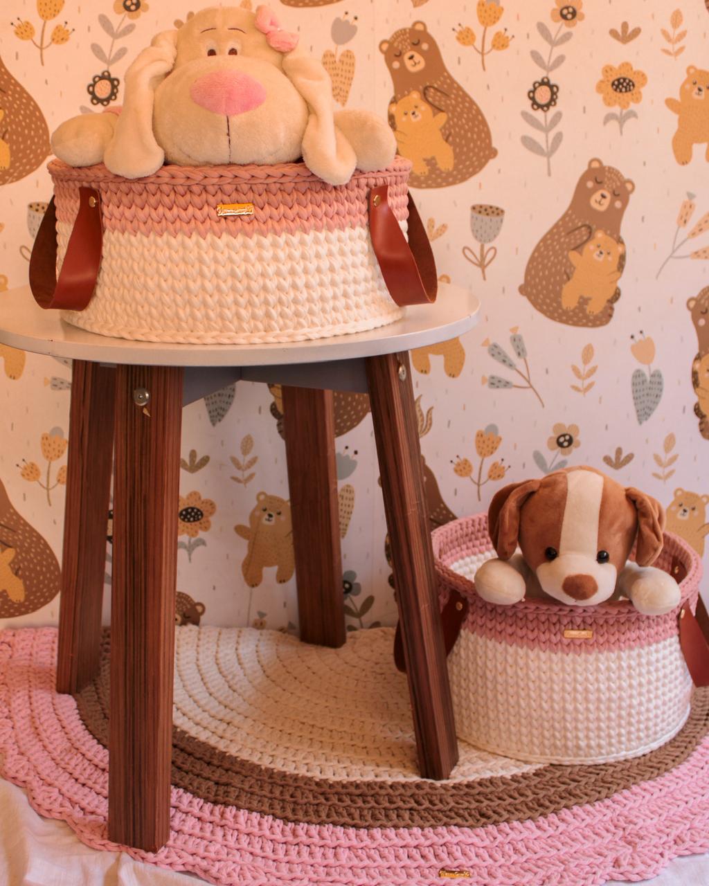 Foto de uma mulher loira sentada no ch&atilde;o. Ela toca um tapete infantil de croch&ecirc; rosa, marrom e branco. Tamb&eacute;m h&aacute; caixas redondas com o mesmo material