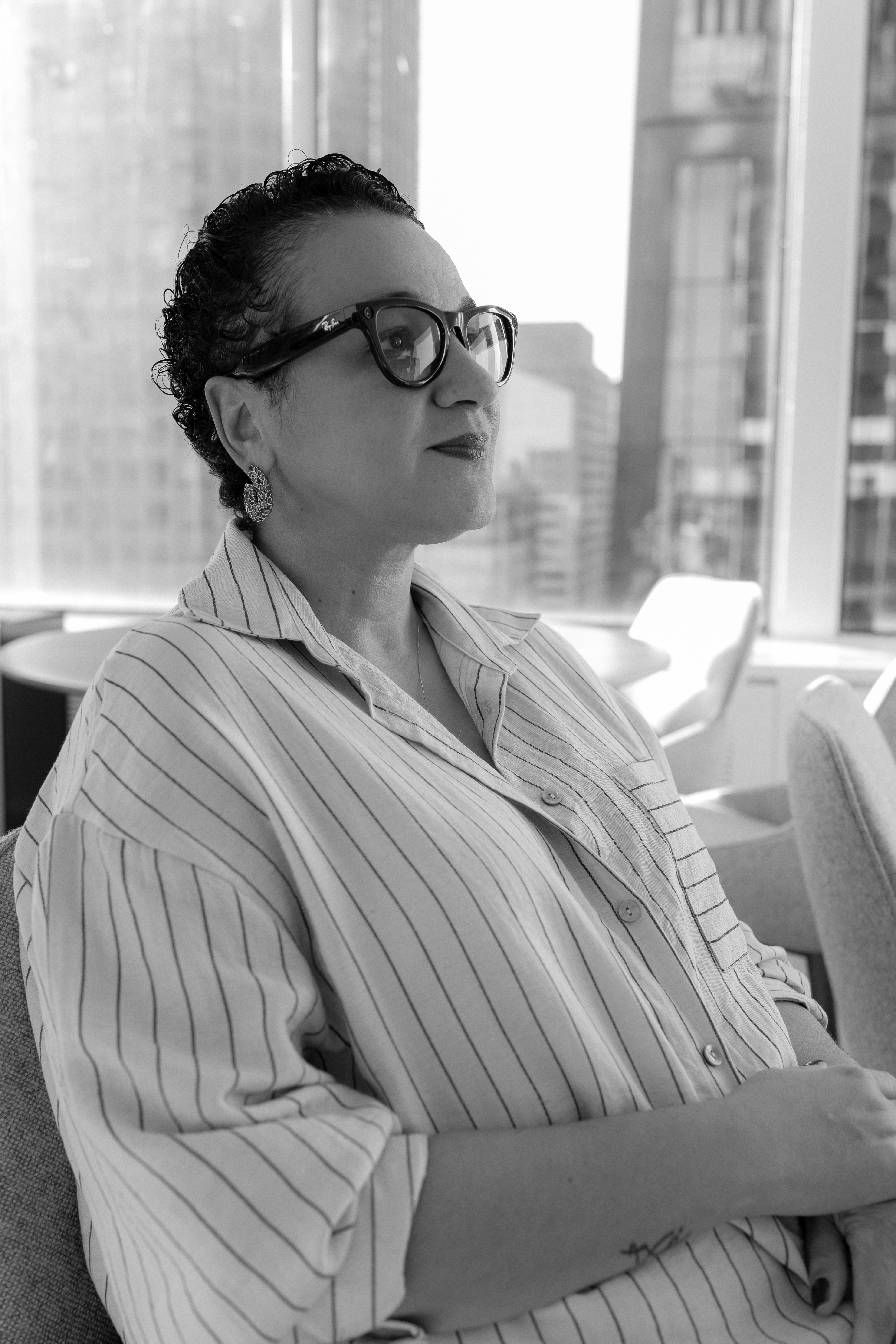 Foto em preto e branco de Tarciana Medeiros. Ela &eacute; morena, tem cabelo curto e cacheado, usa &oacute;culos de grau e uma camisa listrada