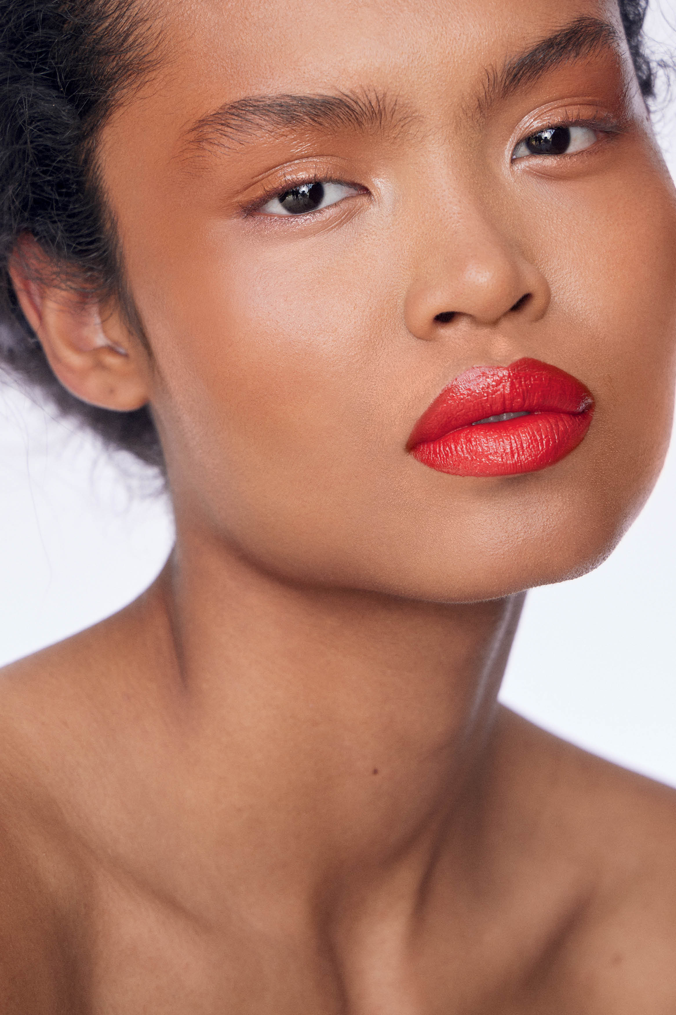 Close no rosto de modelo de pele negra usando maquiagem com cores quentes e batom vermelho