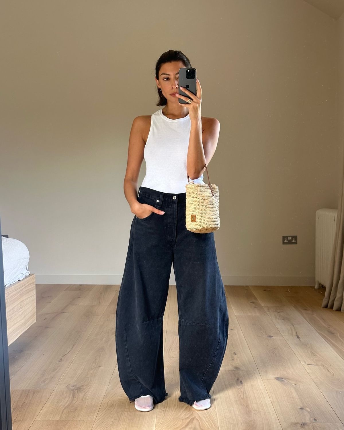 Foto de uma mulher morena usando um look composto por regata branca, cal&ccedil;a jeans ballon e bolsa