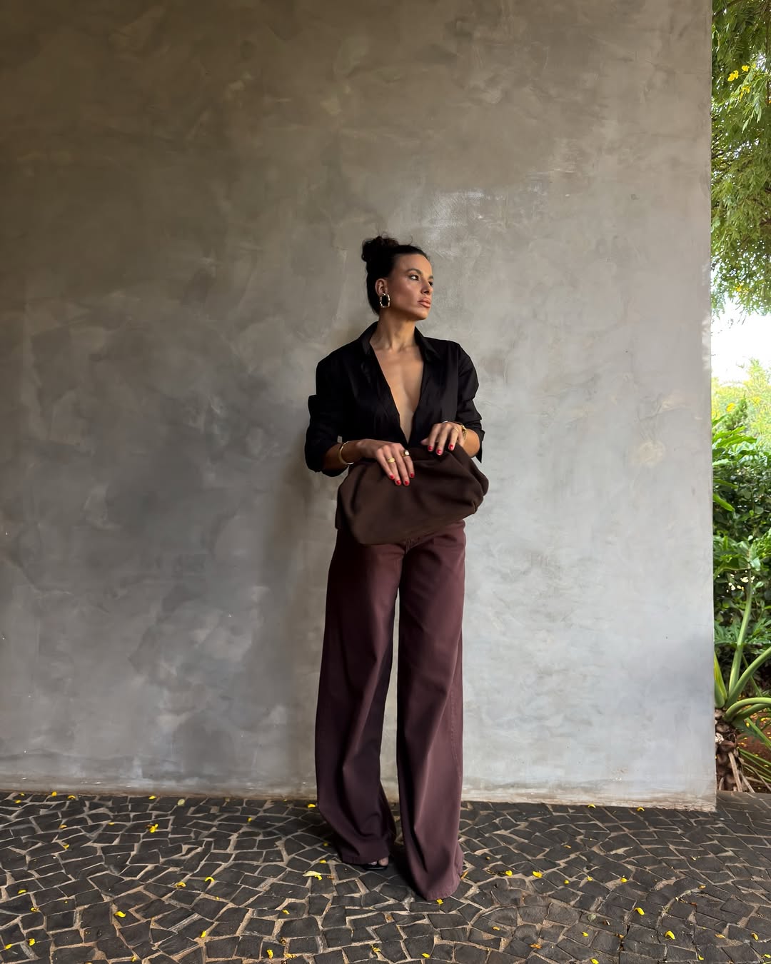 Foto de uma mulher usando uma blusa decotada preta, cal&ccedil;a marrom e bolsa marrom