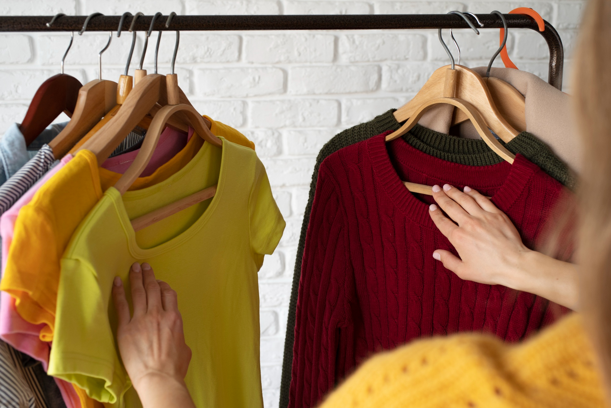 Pessoa escolhendo roupas coloridas em cabideiro com destaque para pe&ccedil;as vermelha e amarela, imagem sobre como as cores do guarda-roupa podem transmitir autoconfian&ccedil;a e presen&ccedil;a em 2026