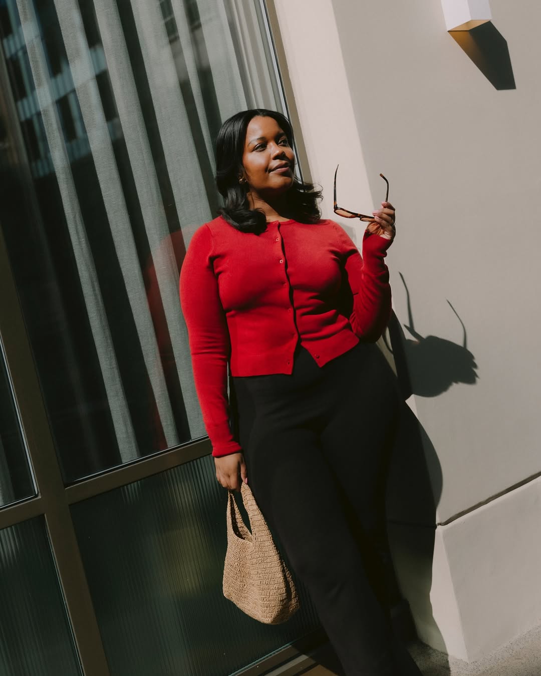 Foto de uma mulher negra usando um look composto por blusa vermelha, cal&ccedil;a legging e bolsa de palha